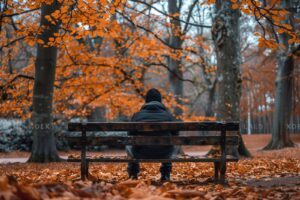 Personne seule assise sur un banc dans un parc en automne pour illustrer la Journée Mondiale des Solitudes